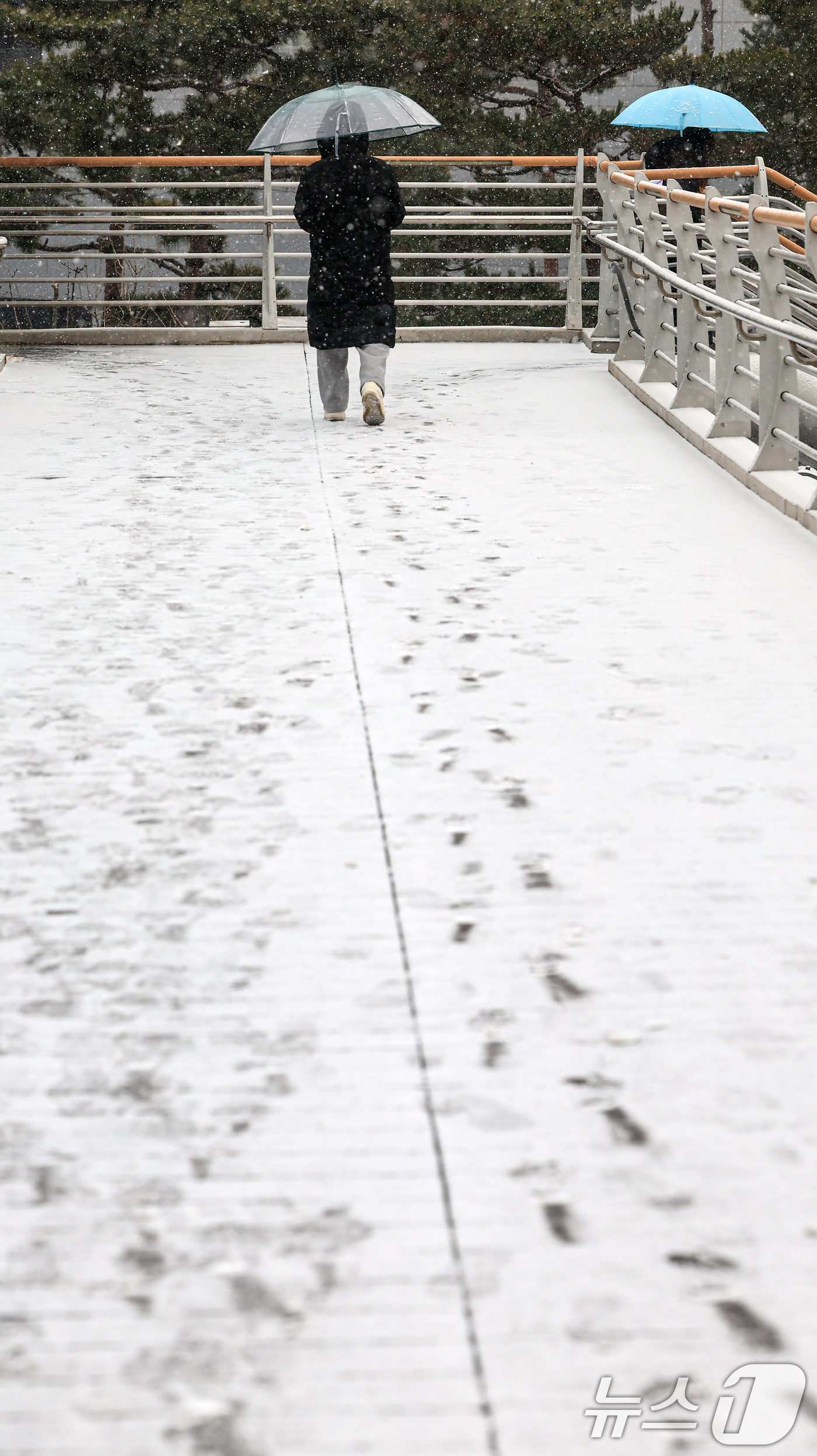 (서울=뉴스1) 이호윤 기자 = 눈이 내리는 12일 서울 마포구 인근 육교에 시민들이 우산을 쓰고 발걸음을 옮기고 있다. 2026.1.12/뉴스1
