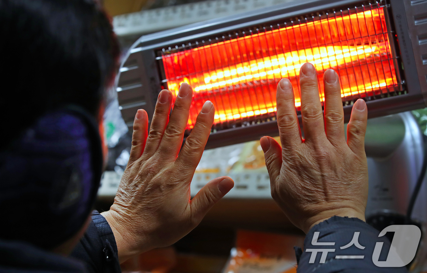 (대구=뉴스1) 공정식 기자 = 매서운 한파가 맹위를 떨친 14일 오전 대구 북구 칠성시장에서 영업을 준비하던 상인이 꽁꽁 언 손을 전기난로에 녹이고 있다. 2026.1.14/뉴스 …