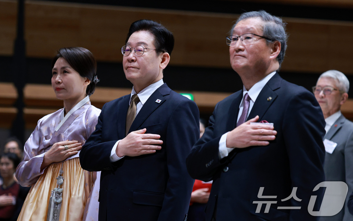 (나라(일본)=뉴스1) 이재명 기자 = 이재명 대통령과 김혜경 여사가 14일 일본 나라현의 한 호텔에서 열린 간사이 동포 간담회에서 국민의례를 하고 있다. 2026.1.14/뉴스1 …
