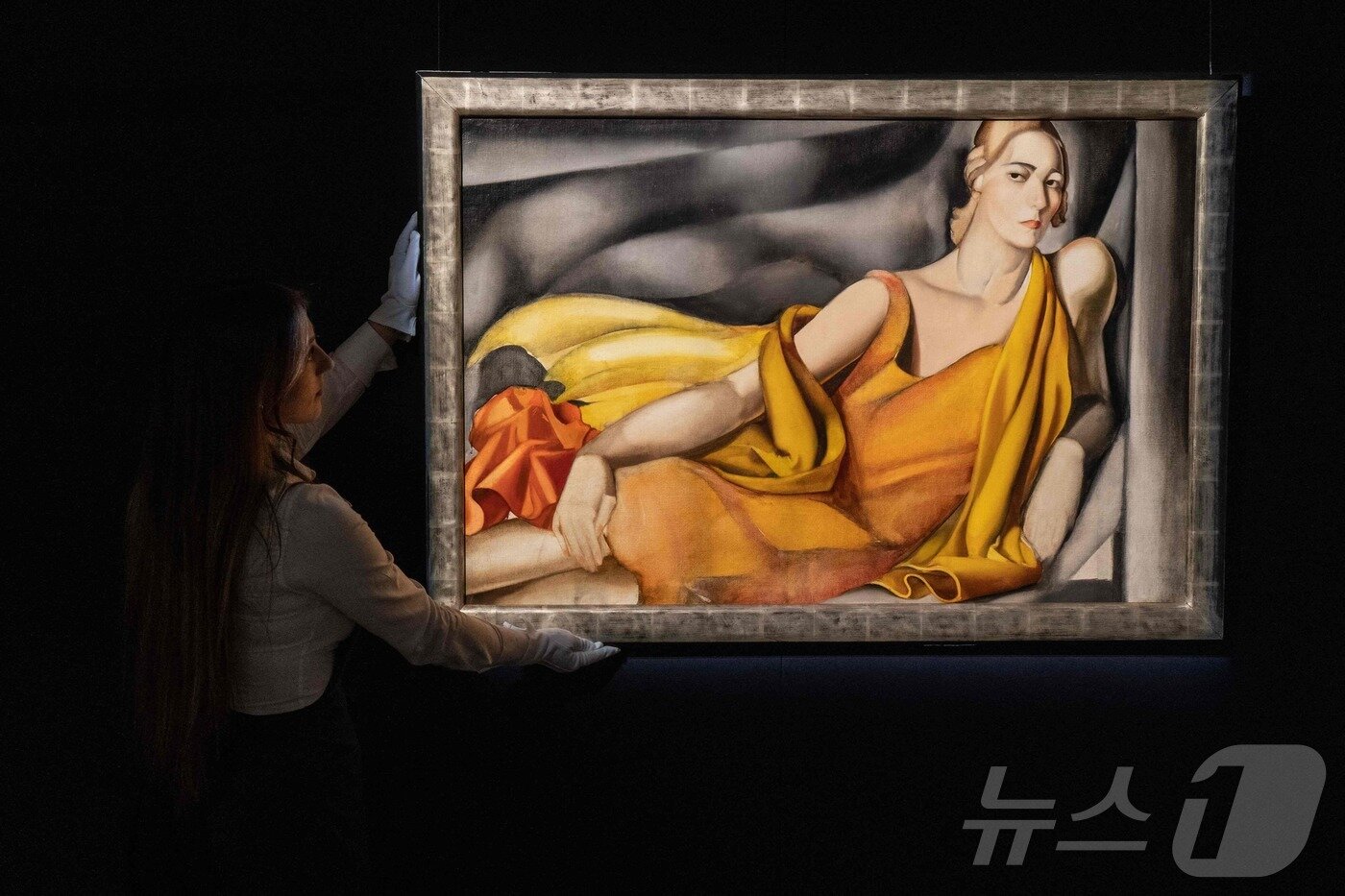 본문 이미지 - 2022년 4월 25일 영국 런던 소더비 경매장에서 열린 프레스 뷰에서, 한 직원이 폴란드 출신 화가 타마라 드 렘피카가 1929년에 제작한 작품 '노란 드레스를 입은 여인'(Femme &agrave; la robe jaune)을 걸고 있다. ⓒ AFP=뉴스1 ⓒ News1  