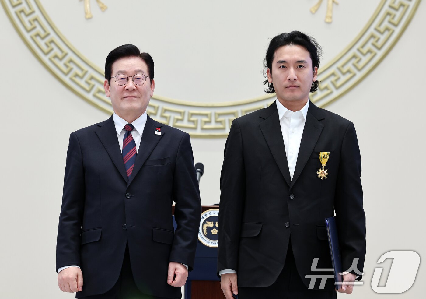 본문 이미지 - 이재명 대통령이 2일 청와대 영빈관에서 열린 2026년 신년 인사회에서 신우석 돌고래유괴단 감독에게 국민훈장 목련장을 수여하고 기념촬영을 하고 있다. 2026.1.2/뉴스1 ⓒ News1 이재명 기자