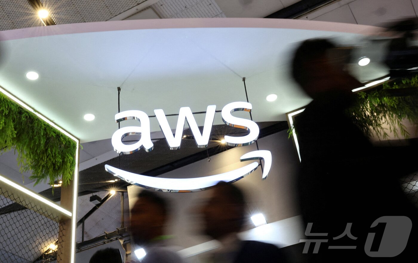 본문 이미지 - 인도 아마존웹서비스. FILE PHOTO: People walk past the logo of Amazon Web Services (AWS) at its exhibitor stall at the India Mobile Congress 2025 at Yashobhoomi, a convention and expo center in New Delhi ⓒ 로이터=뉴스1