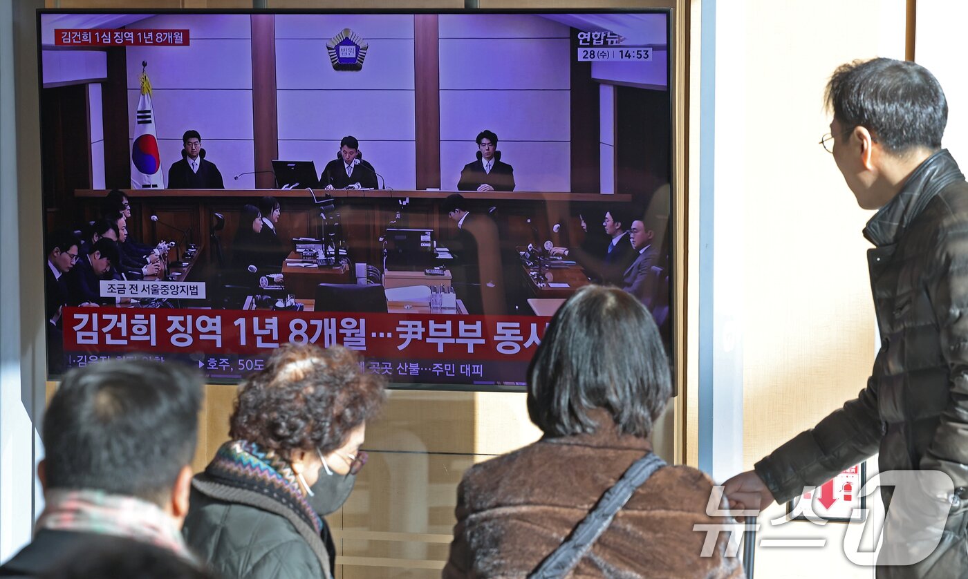 본문 이미지 - 28일 오후 서울역 대합실에서 시민들이 김건희 여사의 자본시장법·정치자금법 위반, 특정범죄 가중처벌법상 알선수재 혐의 1심 선고 공판 생중계를 지켜보고 있다. 서울중앙지법 형사합의27부(부장판사 우인성)는 이날 알선수재 등 혐의로 기소된 김 여사에게 징역 1년 8개월을 선고했다. 압수된 그라프사 다이아몬드 목걸이의 몰수 및 1281만 원의 추징도 명했다. 자본시장법 위반과 정치자금법 위반 혐의에 대해서는 무죄를 선고했다. 2026.1.28/뉴스1 ⓒ News1 오대일 기자