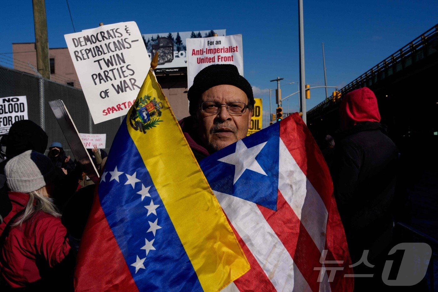본문 이미지 - 4일(현지시간) 뉴욕 브루클린에 있는 메트로폴리탄 구치소 앞에서 열린 미국의 베네수엘라 개입에 항의하고 니콜라스 마두로 베네수엘라 대통령의 석방을 요구하는 시위 현장에서 한 남성이 베네수엘라와 푸에르토리코 국기를 들고 있다. 2026.1.5 ⓒ 로이터=뉴스1