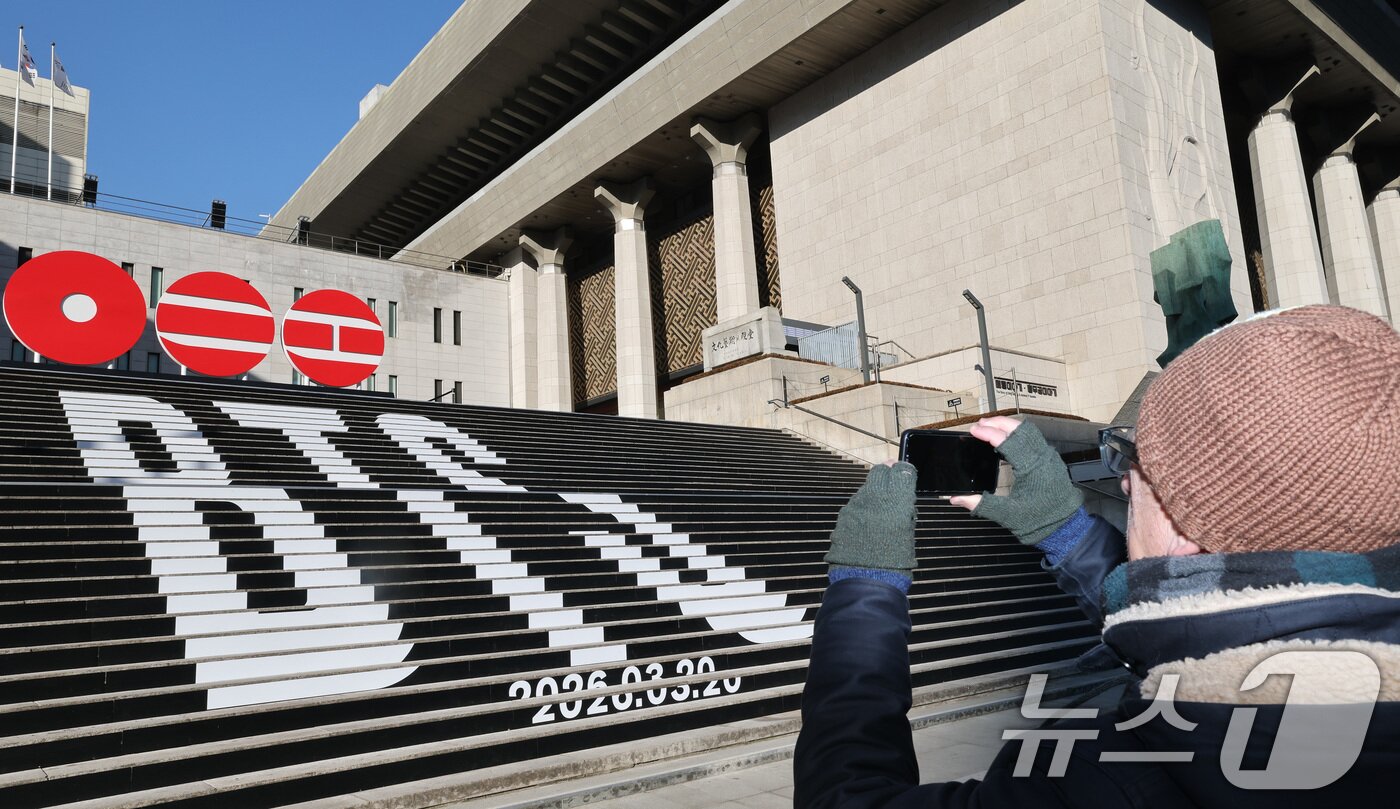 본문 이미지 - 6일 오전 서울 종로구 세종문화회관 야외 계단에 설치된 BTS(방탄소년단)의 컴백 로고 조형물 앞에서 관광객이 기념촬영을 하고 있다. BTS는 3월 20일 컴백과 새 앨범 발매, 월드투어 일정을 공식 발표했다. 2026.1.6/뉴스1 ⓒ News1 임세영 기자