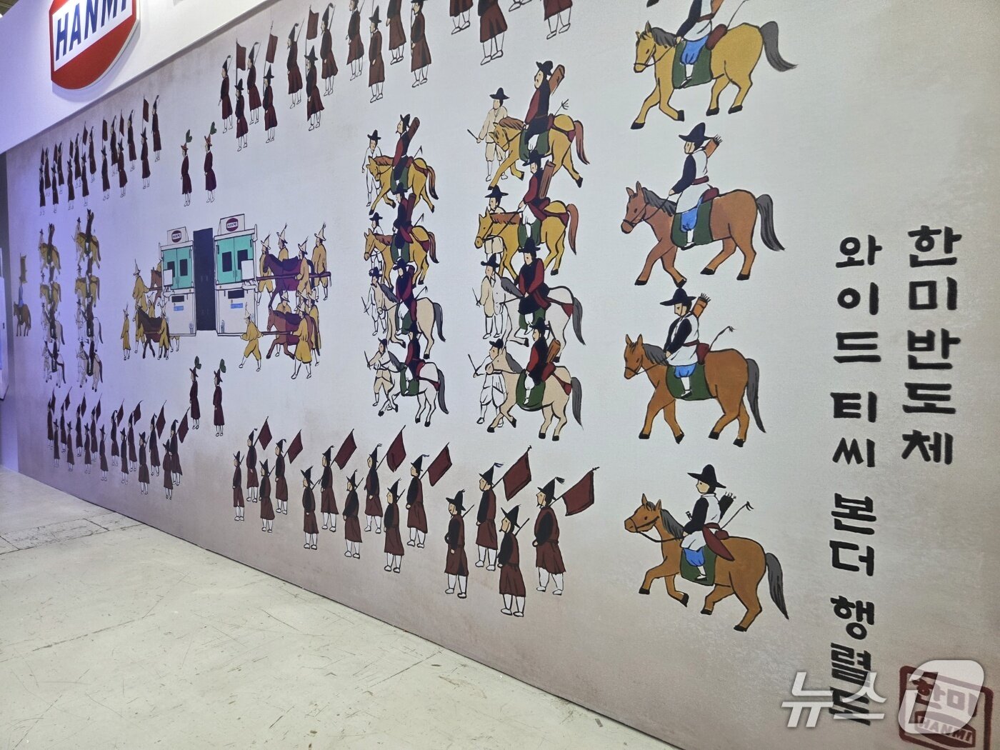 본문 이미지 - 한미반도체가 '반도체대전 2026'에 설치한 홍보부스 한쪽 벽면에 그린 패러디 행렬도를 통해 반도체 장비 'TC-본더'를 소개하고 있다. 2026. 10. 14/뉴스1 황진중 기자
