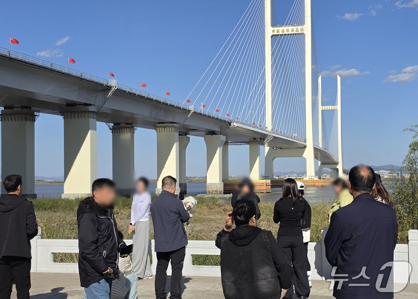 본문 이미지 - 신압록강대교 정식 개통을 하루 앞둔 14일 중국 랴오닝성 단둥의 대교 인근에 관광객들이 모여 있다. 뒤로 보이는 대교 중국 측 구간에는 오성홍기가 줄지어 내걸려 있다. 2026.10.14. ⓒ 단둥=뉴스1 노민호 특파원