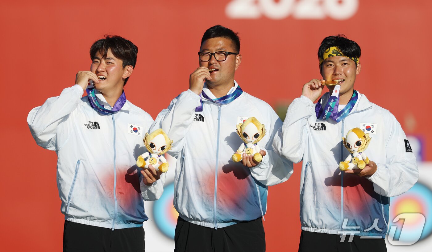 본문 이미지 - 대한민국 김제덕(왼쪽부터), 김우진, 이우석이 2일 일본 오카자키 중앙종합공원 다목적광장에서 열린 2026 아이치·나고야 아시안게임 양궁 리커브 남자 단체전 결승 시상식에서 금메달을 깨물고 세리머니를 하고 있다. 2026.10.2 ⓒ 뉴스1 김민지 기자