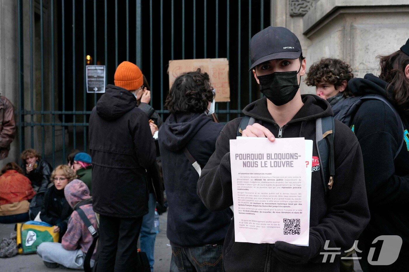 본문 이미지 - 19일(현지시간) '에콜 뒤 루브르'(&Eacute;cole du Louvre) 학생을 비롯한 시위대가 고등학생 시위대에 대한 지지를 표명하며 프랑스 파리 루브르 박물관 입구를 막아선 가운데, 한 청년이 방문객들에게 폐관을 알리는 플래카드를 들어 보이고 있다. 2026.10.19. ⓒ AFP=뉴스1