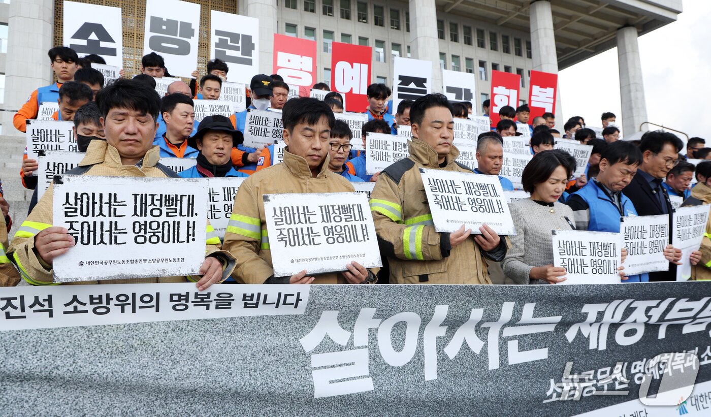 본문 이미지 - 21일 서울 영등포구 여의도 국회의사당 계단에서 열린 대한민국공무원노동조합총연맹 소방공무원노동조합원들이 소방공무원 명예회복과 소방조직 정상화 촉구 기자회견에서 희생된 소방관들에 대한 묵념을 하고 있다. 2026.10.21 ⓒ 뉴스1 김명섭 기자