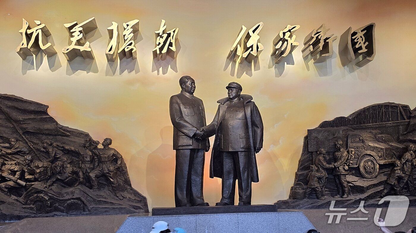 본문 이미지 - 중국인민지원군의 한국전쟁 참전 76주년인 25일 중국 단둥 '항미원조기념관' 내에 마오쩌둥 전 중국 국가주석(왼쪽)과 펑더화이 당시 중국인민지원군 사령관이 악수하는 동상이 세워져 있다. 뒤편에는 '미국에 맞서 북한을 돕고 가정과 나라를 지킨다'는 뜻의 '항미원조 보가위국'(抗美援朝 保家衛國) 문구가 걸려 있다. 이곳은 전날 김정은 북한 노동당 총비서가 방문한 곳이다. 2026.10.25 ⓒ 뉴스1 노민호 특파원