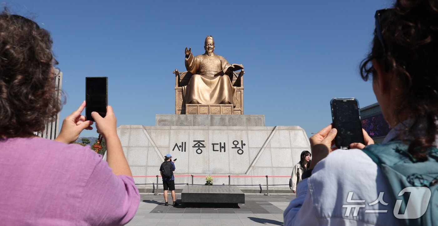 본문 이미지 - 한글날 제정 100주년을 하루 앞둔 8일 서울 종로구 광화문광장에서 외국인 관광객들이 세종대왕 동상을 스마트폰에 담고 있다. 올해는 훈민정음 반포 580주년이자 한글날 제정 100주년을 맞는 해다. 2026.10.8 ⓒ 뉴스1 박지혜 기자