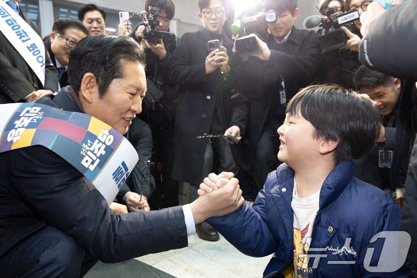 본문 이미지 - 정청래 더불어민주당 대표가 13일 서울 용산역에서 설 귀성객 인사를 하며 아이와 팔씨름을 하고 있다. 2026.2.13 ⓒ 뉴스1 이승배 기자
