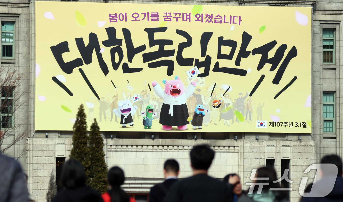 본문 이미지 - 제107주년 삼일절을 앞둔 27일 서울 중구 서울도서관 벽면에 '봄이 오기를 꿈꾸며 외쳤습니다, 대한독립만세'라는 서울꿈새김판이 걸려 있다. 서울 꿈새김판은 서울도서관 외벽의 대형 글판이다. 흩날리는 꽃잎 가운데 태극기를 힘차게 흔들며 만세를 외치는 독립운동가의 이미지를 표현했다. 2026.2.27 ⓒ 뉴스1 김명섭 기자