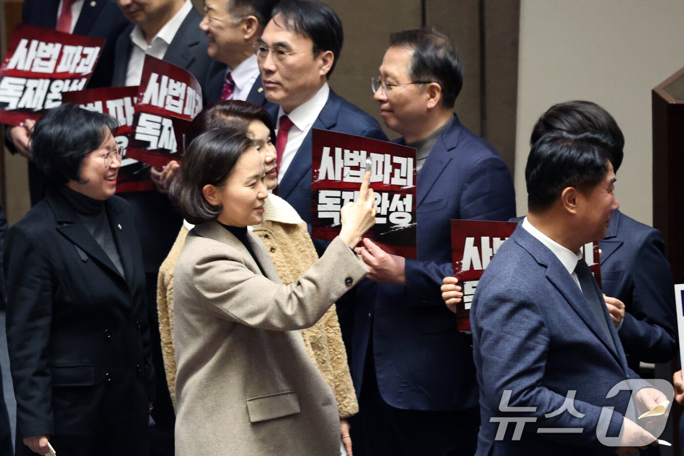 본문 이미지 - 27일 서울 여의도 국회에서 열린 제432회 국회(임시회) 제8차 본회의에서 재판소원제 도입을 골자로 하는 헌법재판소법 일부개정법률안(대안)에 대한 무제한토론 종결 투표가 진행되는 가운데 이해민 조국혁신당 의원이 사법 3법과 관련 규탄 피켓 농성하는 국민의힘 의원들을 핸드폰에 담고 있다. 2026.2.27 ⓒ 뉴스1 이승배 기자