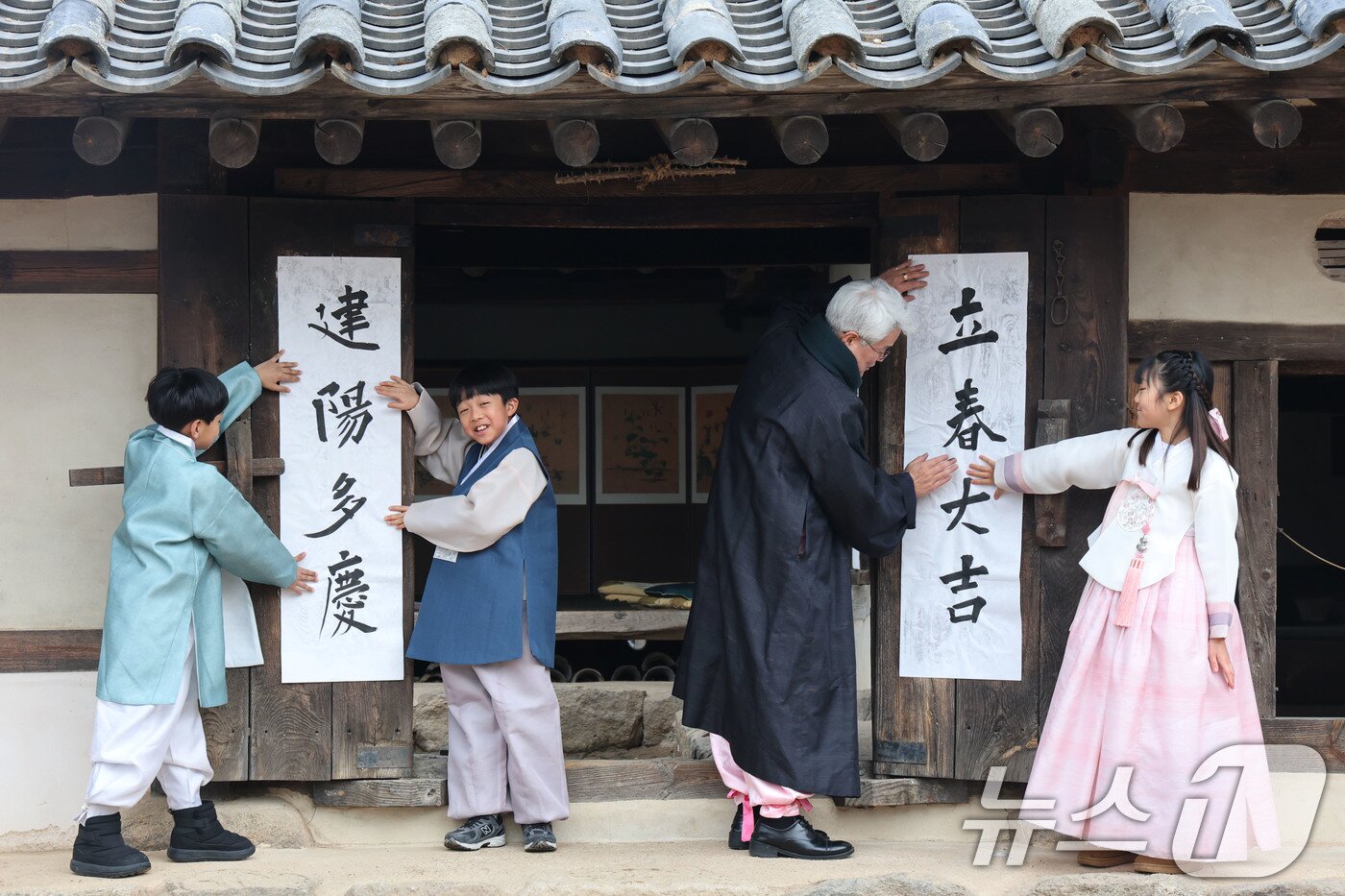 본문 이미지 - 봄의 시작을 알리는 입춘(立春)인 4일 서울 종로구 삼청동 국립민속박물관내 전통한옥인 오촌댁 대문에 어린이들이 '입춘대길(立春大吉)'과 '건양다경(建陽多慶)' 글귀를 담은 입춘첩을 붙이고 있다.  2026.2.4/뉴스1 ⓒ News1 이광호 기자