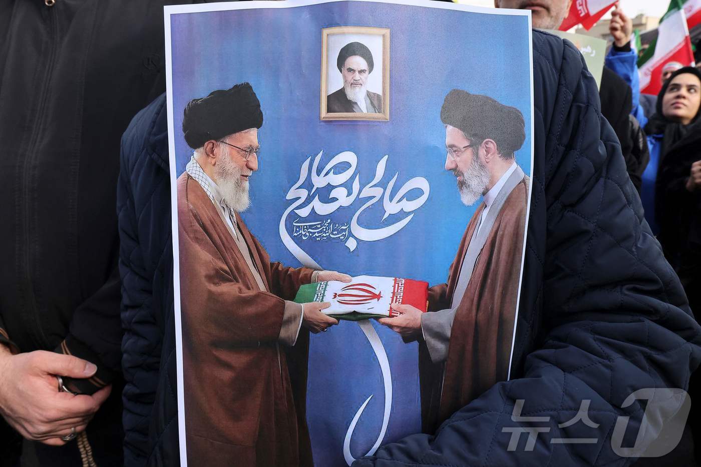 테헤란 (AFP=뉴스1) 이정환 기자 = 9일(현지시간) 이란 테헤란 중심부 엥겔랍 광장에서 열린 친정부 집회에서 한 남성이 이란 최고지도자 아야톨라 알리 하메네이(왼쪽)가 차남 …