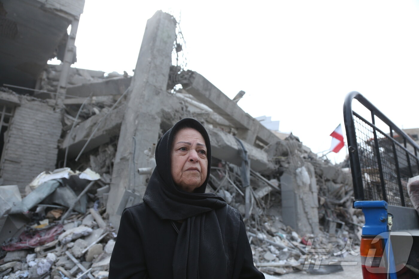 본문 이미지 - 지난 12일(현지시간) 이란 수도 테헤란의 무너진 건물 앞에서 한 여성이 허망한 표정으로 서 있다.ⓒ 신화=뉴스1