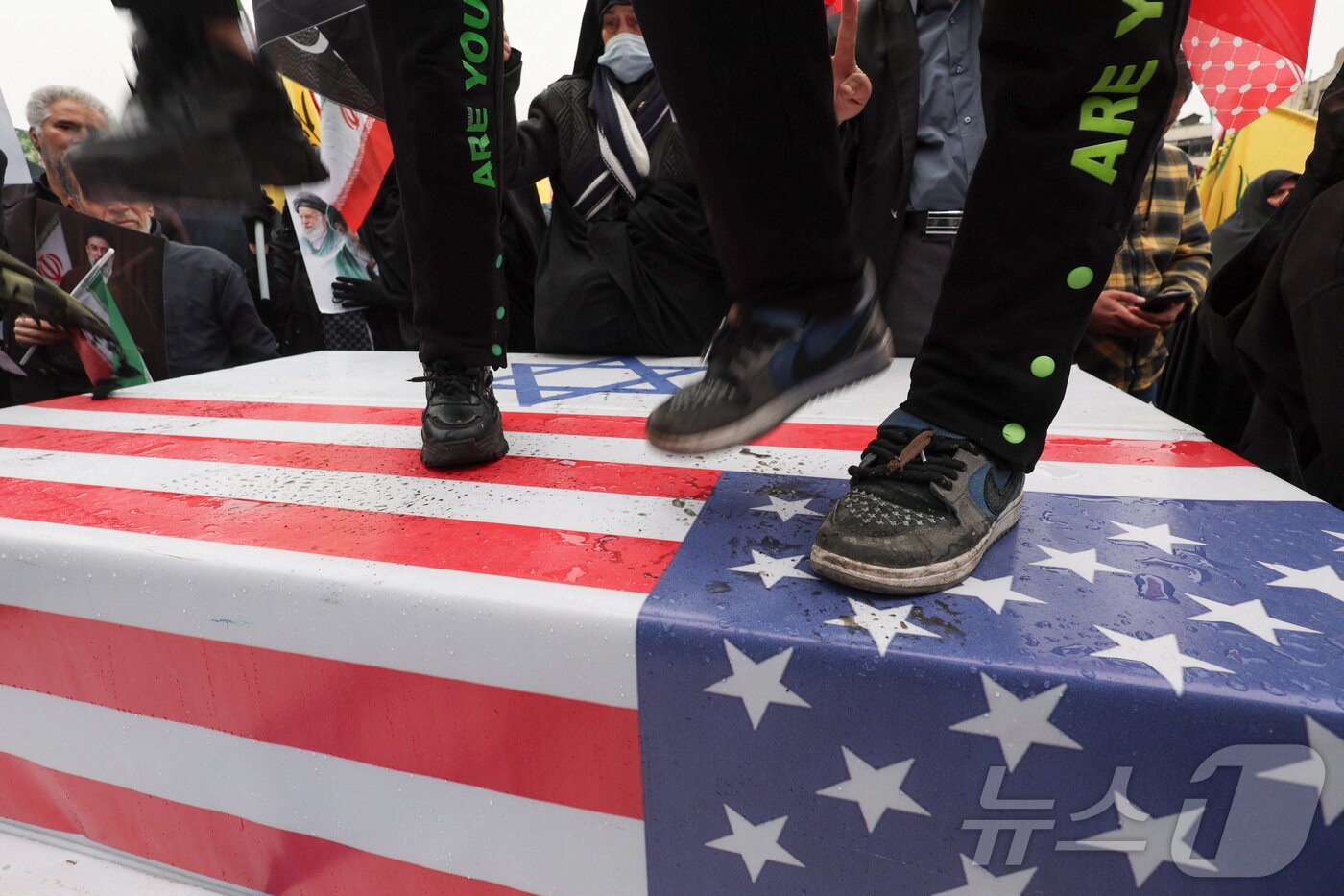 본문 이미지 - 미국-이스라엘 국기 짓밟는 이란 테헤란의 시위대. 2026.03.13 ⓒ 로이터=뉴스1