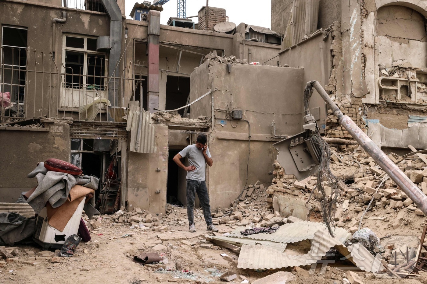 (테헤란 AFP=뉴스1) 이정환 기자 = 15일(현지시간) 이란 수도 테헤란에 대한 군사 공습 이후, 한 남성이 파손된 주택들 밖에서 휴대전화로 통화하고 있다. 2026.03.15 …