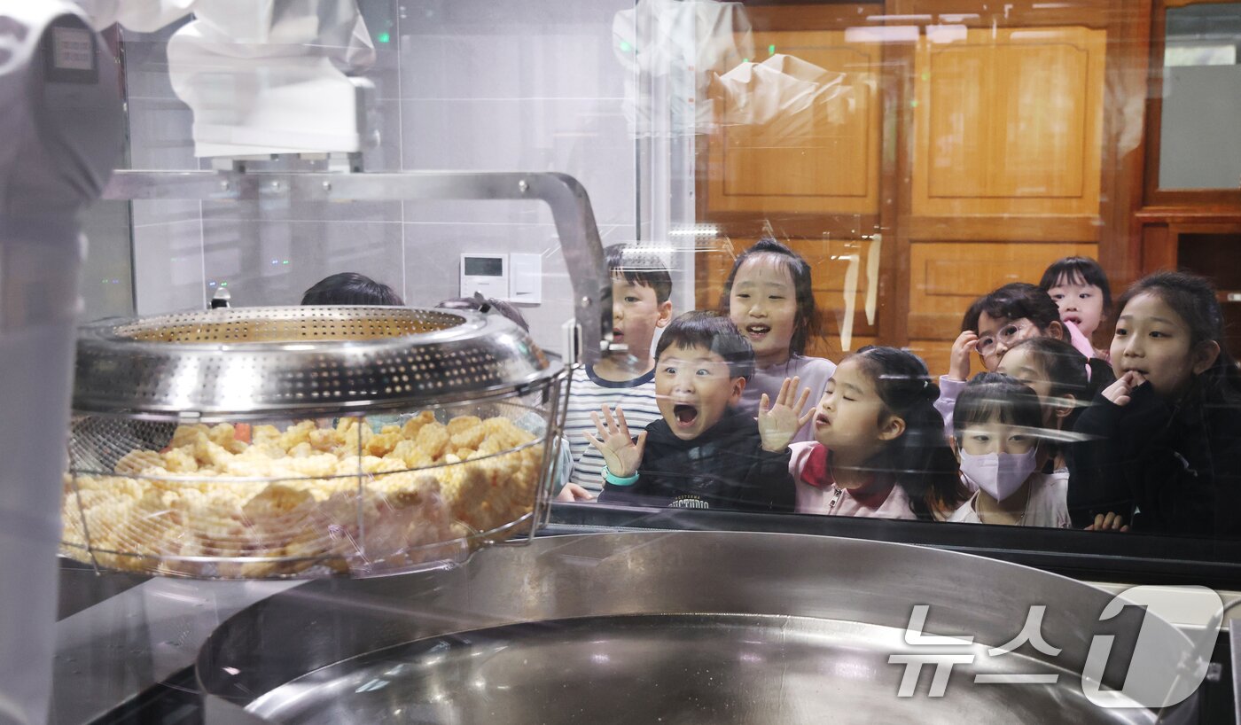 본문 이미지 - 18일 경기 수원시 장안구 대평초등학교 내 위치한 거점형 학교급식 튀김 지원실에서 1학년 학생들이 튀김 조리 로봇이 직접 가동되는 현장을 보고 있다.  2026.3.18 ⓒ 뉴스1 김영운 기자