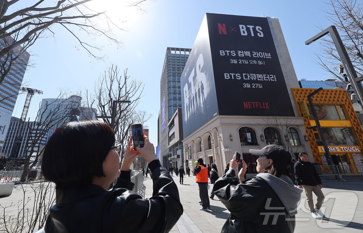 본문 이미지 - 방탄소년단(BTS)의 서울 광화문광장 컴백 공연이 이틀 앞으로 다가온 19일 서울 종로구 광화문광장에서 시민들이 한 건물 외벽에 부착된 BTS 컴백 공연 광고물을 스마트폰으로 촬영하고 있다. 2026.3.19 ⓒ 뉴스1 김성진 기자