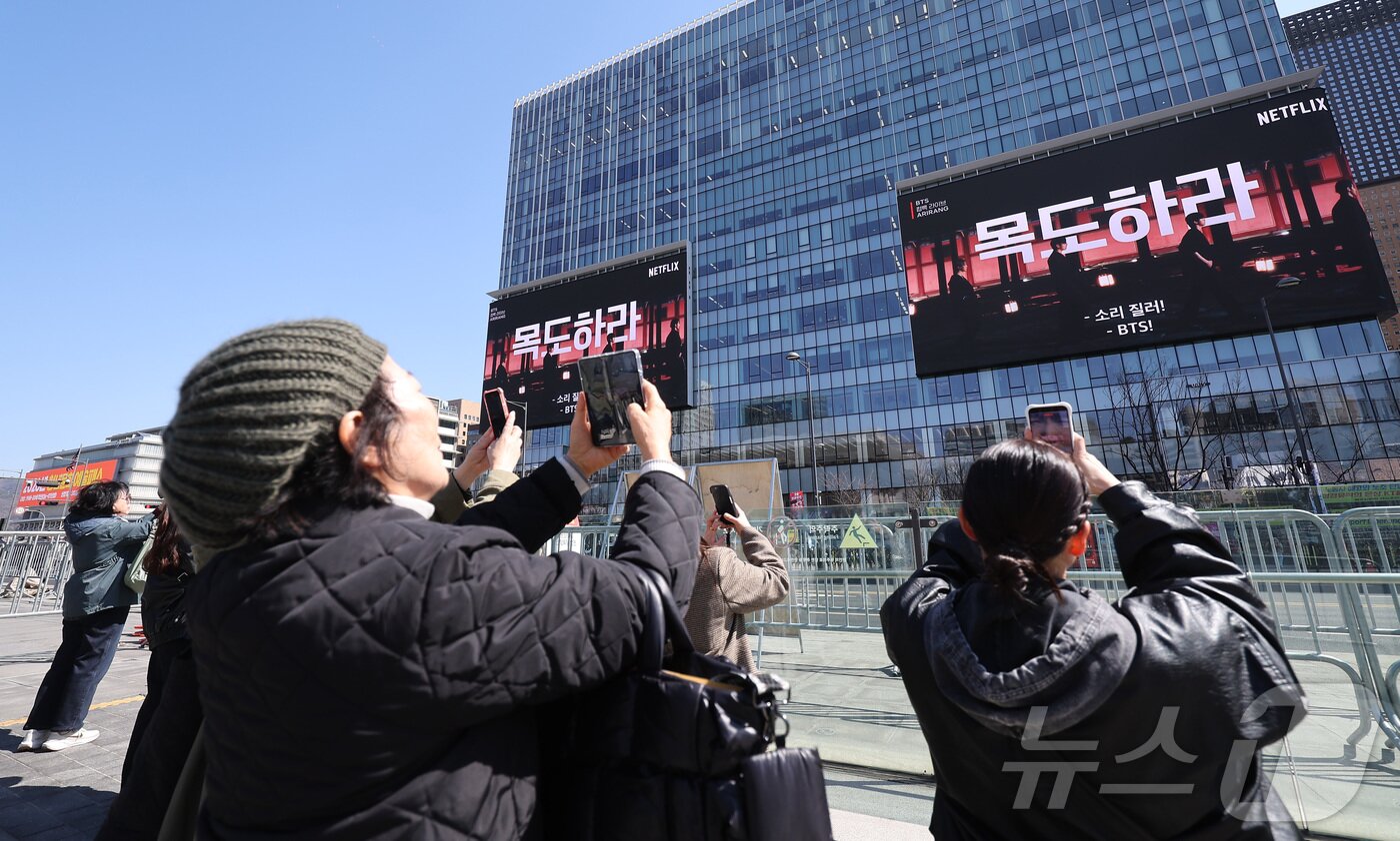 본문 이미지 - 방탄소년단(BTS)의 서울 광화문광장 컴백 공연이 이틀 앞으로 다가온 19일 서울 종로구 광화문광장에서 외국인 팬들이 컴백 공연을 알리는 전광판 광고를 스마트폰으로 촬영하고 있다. 2026.3.19 ⓒ 뉴스1 김성진 기자
