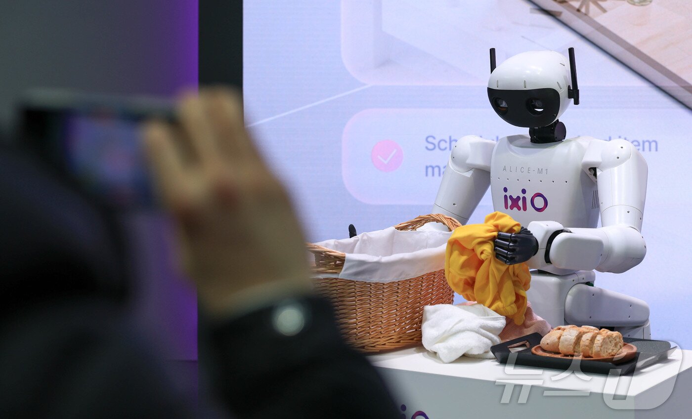 본문 이미지 - 2일(현지시간) 스페인 바르셀로나 피라 그란 비아 전시장에서 열린 '모바일 월드 콩그레스(MWC)2026'에서 LG유플러스 부스에서 AI에이전트 ‘익시오’가 그린 미래를 시연하는 로봇이 빨래를 바구니에 넣고 있다. 2026.3.2 ⓒ 뉴스1 사진공동취재단