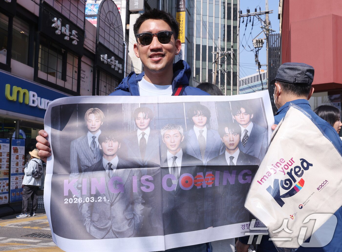 본문 이미지 - 방탄소년단(BTS) 컴백 공연일인 21일 오전 서울 광화문광장 인근에서 외국인 관광객이 BTS 관련 특별판을 들고 기념촬영을 하고 있다. 2026.3.21 ⓒ 뉴스1 박지혜 기자