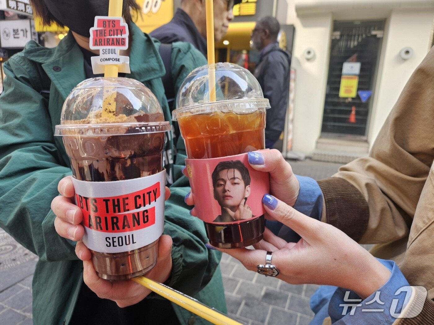 본문 이미지 - 23일 오전 외국인 관광객들이 BTS 멤버 뷔의 사진이 인쇄된 커피를 들고 있다. 2026.3.23 ⓒ 뉴스1 유채연 기자