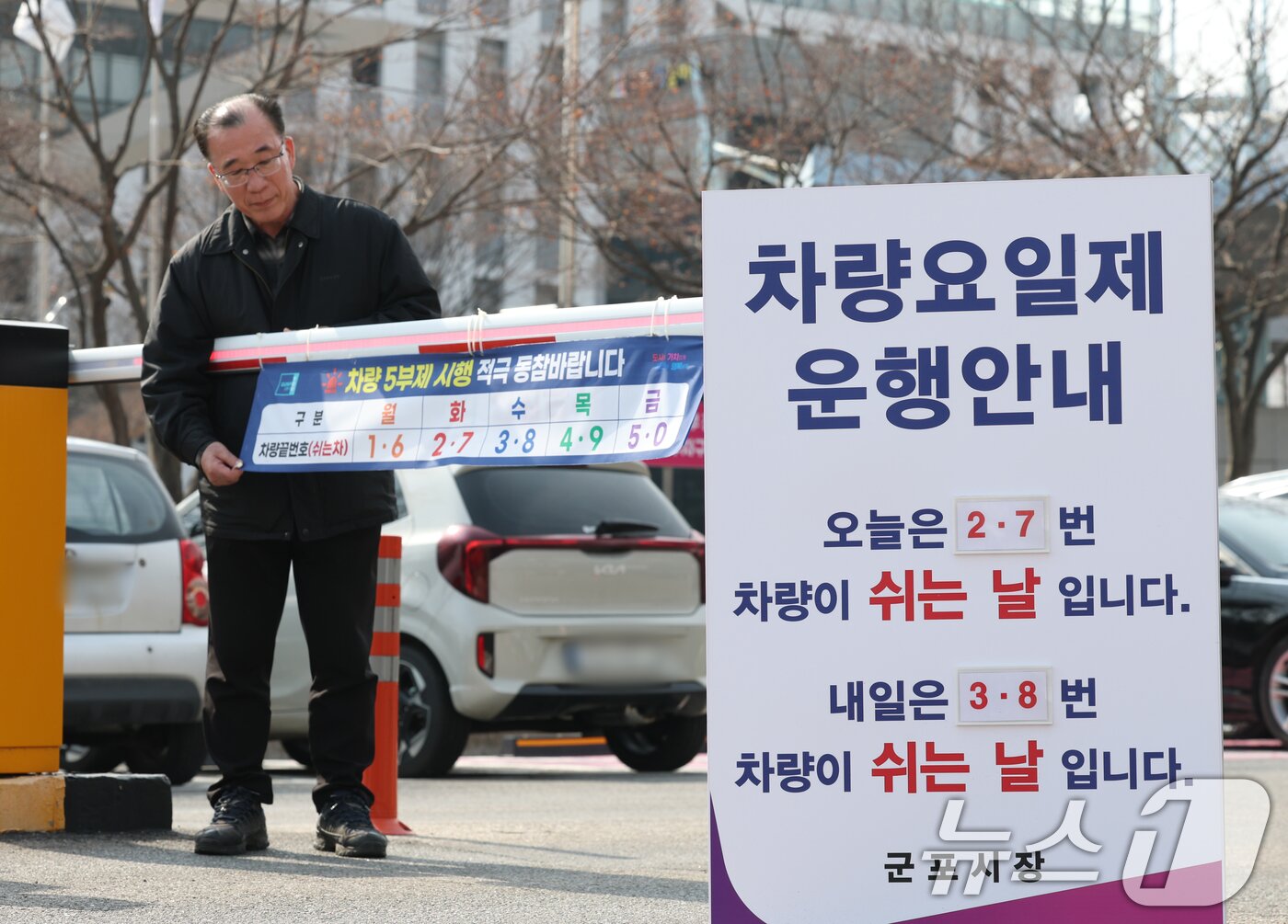 본문 이미지 - 에너지 수급 위기 대응으로 공공부문 차량 5부제 전면 시행을 하루 앞둔 가운데 24일 경기 군포시 금정동 군포시청 직원주차장에서 관계자들이 차량 5부제 시행 현수막을 부착하고 있다.  2026.3.24 ⓒ 뉴스1 김영운 기자
