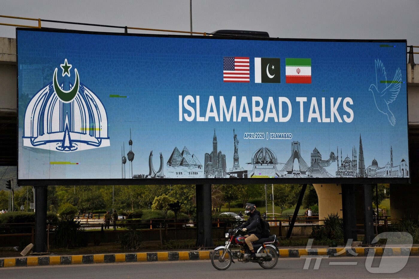 본문 이미지 - 파키스탄이 미국과 이란의 평화 회담 개최를 준비하는 가운데 10일 파키스탄 이슬라마바드에서 한 남성이 도로변에 설치된 광고판 앞을 오토바이를 타고 지나가고 있다. 2026.4.10 ⓒ 로이터=뉴스1