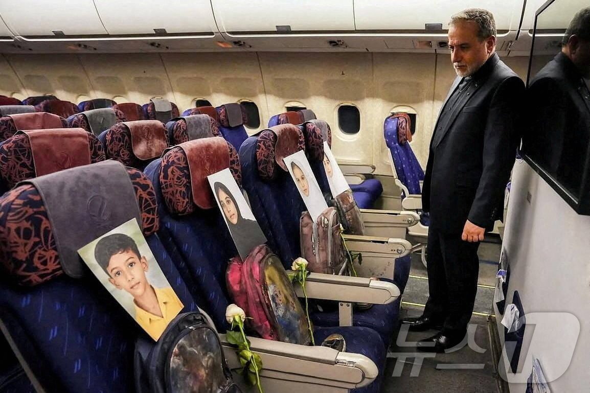 본문 이미지 - 아바스 아라그치 이란 외무장관의 미국과의 협상장으로 향하는 기내로 추정되는 장소에서 미국-이스라엘 공습으로 희생된 어린이들의 영정 사진과 유품을 바라보고 있다. 2026.04.11 ⓒ 로이터=뉴스1