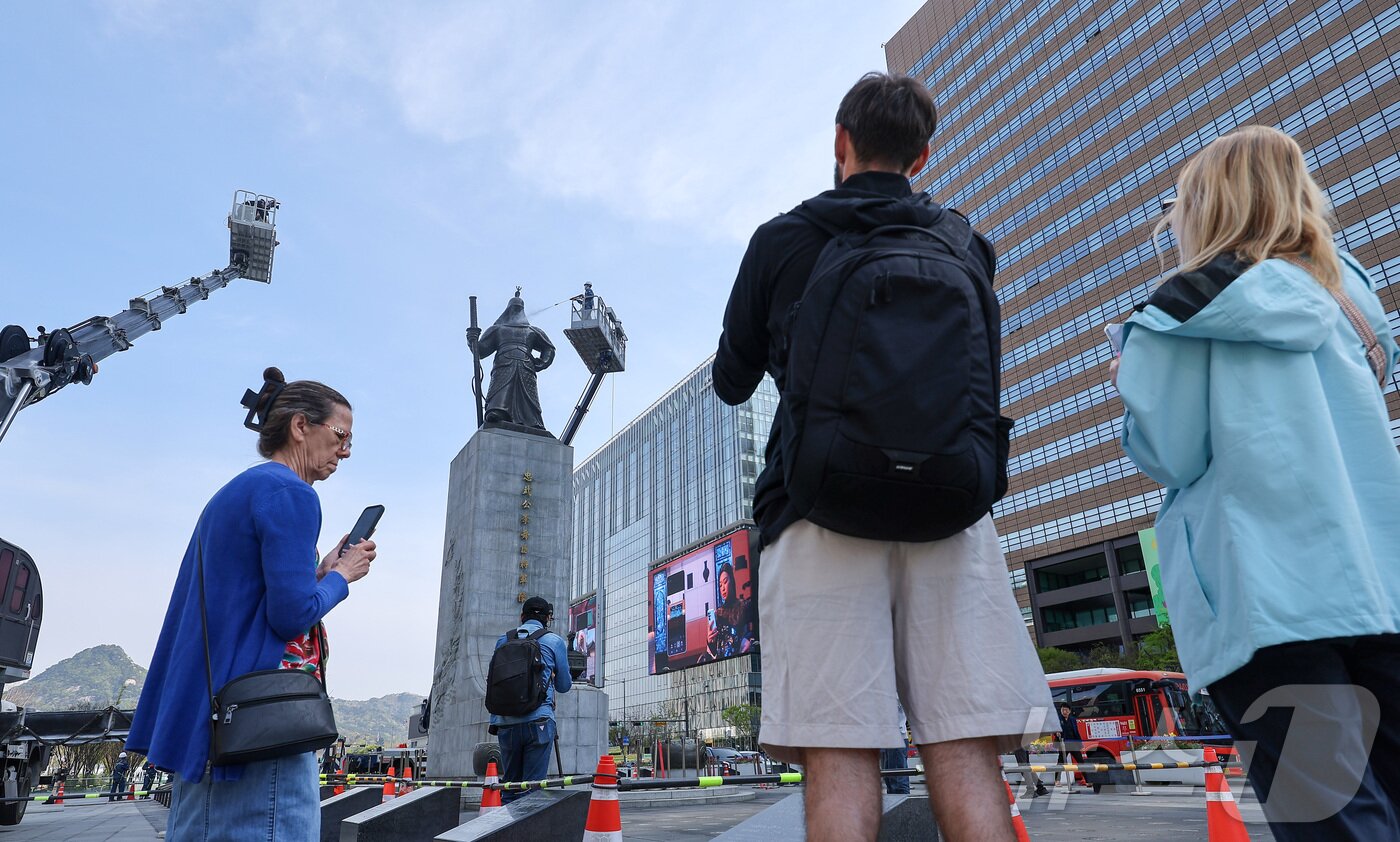 본문 이미지 - 서울시 관계자들이 14일 서울 종로구 광화문광장에서 이순신 장군 동상을 세척 작업이 진행되는 가운데 외국인 관광객들이 이 모습을 지켜보고 있다. 2026.4.14 ⓒ 뉴스1 김성진 기자