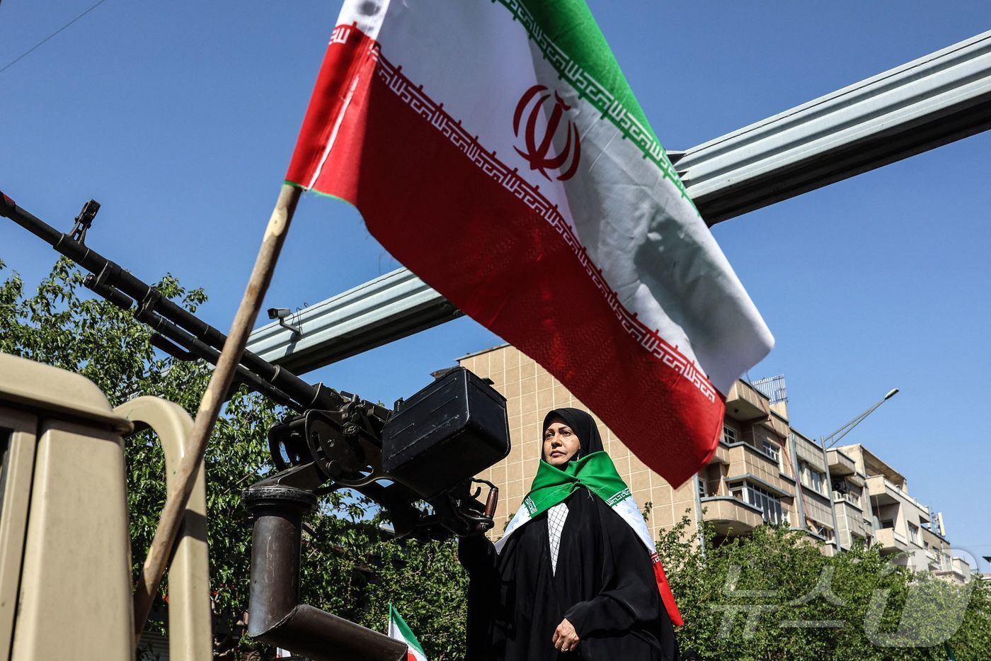 본문 이미지 - 17일(현지시간) 이란 수도 테헤란에서 열린 '희생된 소녀들' 집회에 참가한 한 이란 여성이 차량 뒤에 장착된 중기관총 앞에 서 있다. 2026.04.18. ⓒ AFP=뉴스1