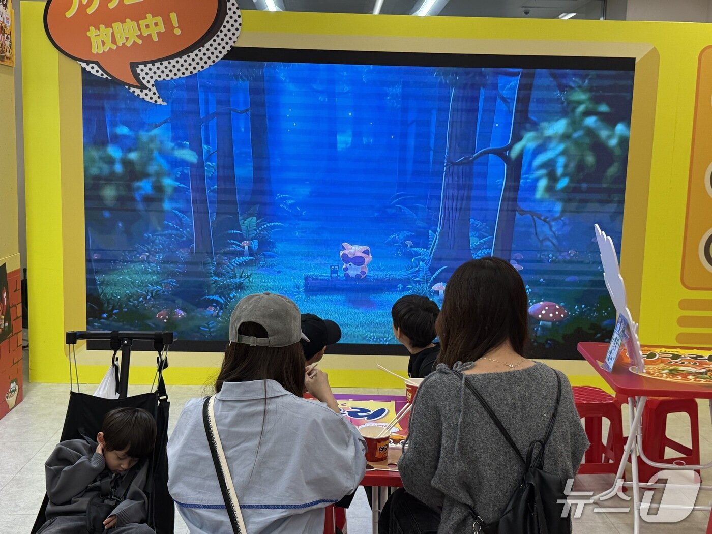 본문 이미지 - 너구리 제품을 시식 중인 가족 단위 방문객이 대형 화면에서 나오는 너구리 애니메이션 영상을 보고 있다. 뉴스1 ⓒ News1 황두현 기자