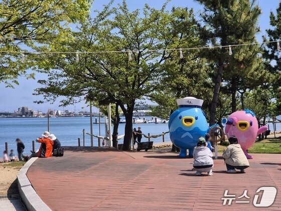 본문 이미지 - 토요일인 25일 강원 속초시 청초호를 찾은 가족 단위 나들이객들이 속초시 캐릭터 '짜니'와 '래요' 앞에서 사진을 찍으며 즐거운 시간을 보내고 있다. 2026.4.25/뉴스1 윤왕근 기자