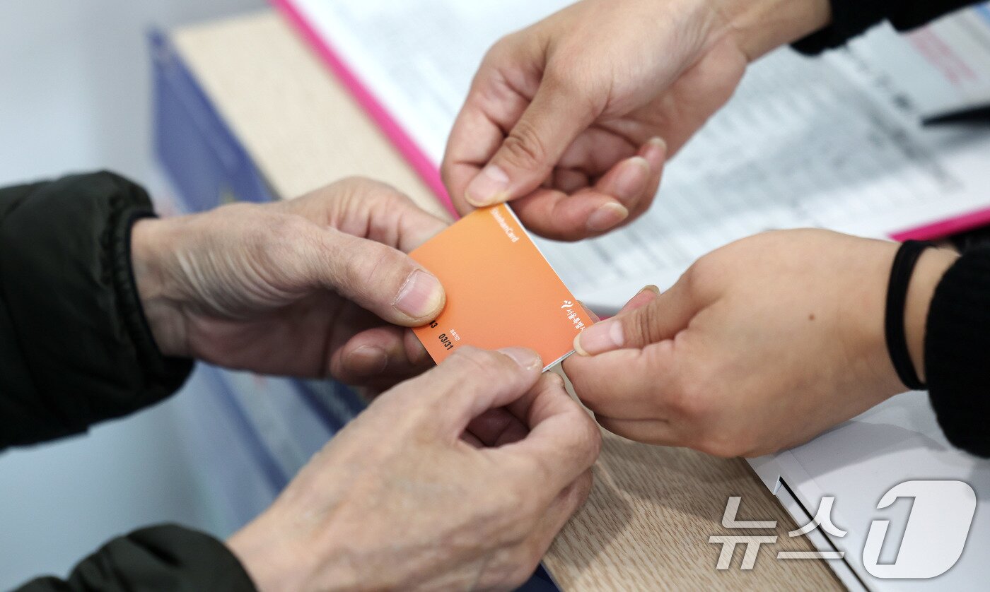 본문 이미지 - 고유가 피해지원금 1차 지급이 시작된 27일 서울 강서구 화곡4동 주민센터에서 직원이 고유가 피해지원금을 시민에게 전달하고 있다. 2026.4.27 ⓒ 뉴스1 박지혜 기자