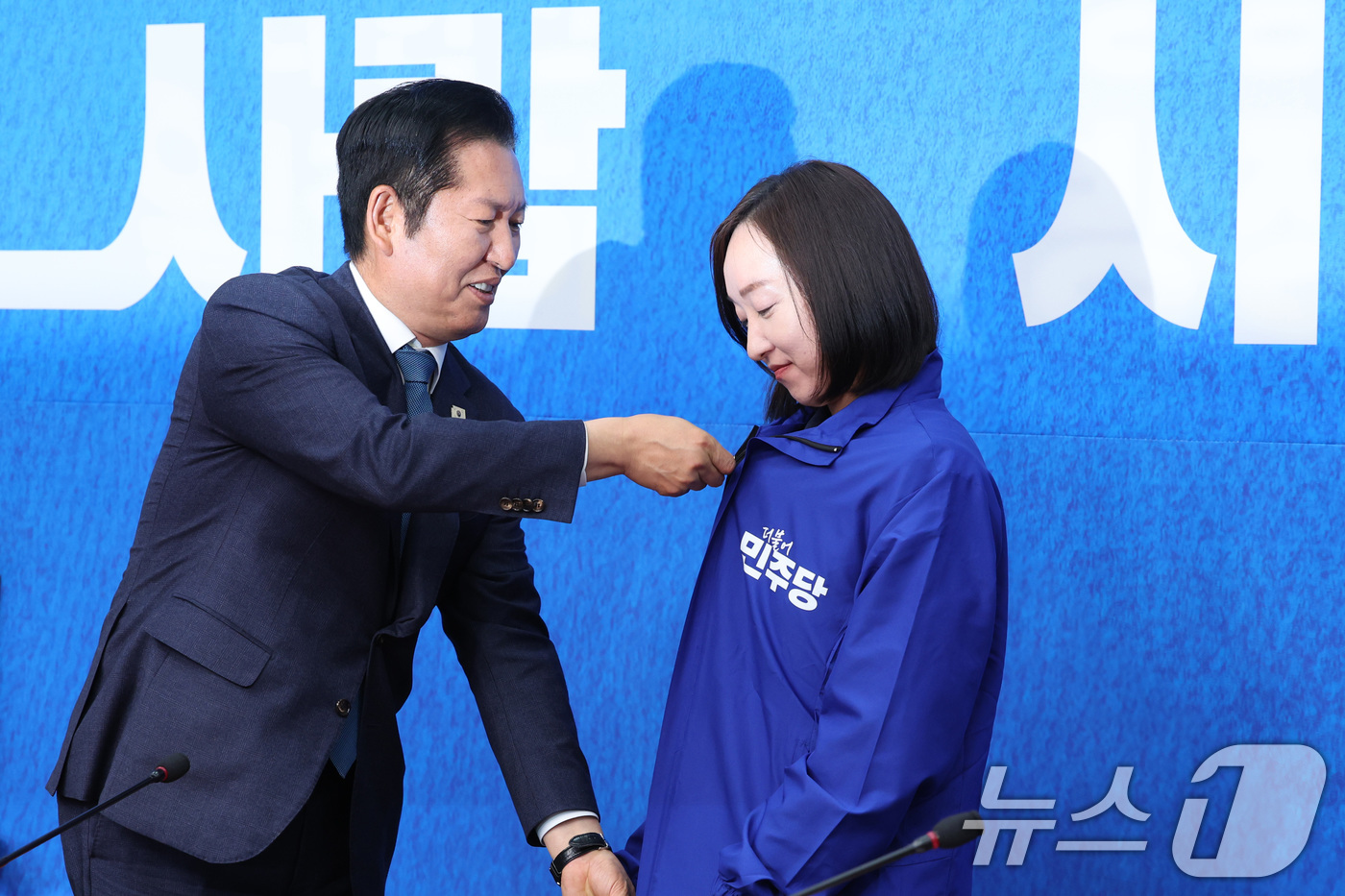 (서울=뉴스1) 신웅수 기자 = 정청래 더불어민주당 대표가 29일 서울 여의도 국회에서 열린 민주당 인재 영입식에서 전은수 전 청와대 대변인에게 당 점퍼를 입혀주고 있다. 2026 …