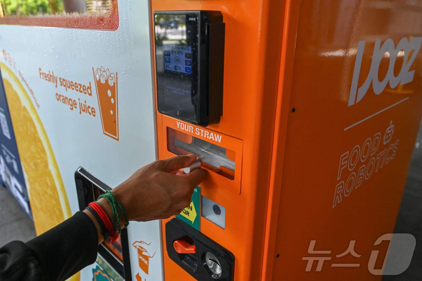 (싱가포르 AFP=뉴스1) 윤다정 기자 = 28일(현지시간) 싱가포르의 한 쇼핑몰 앞에서 한 남성이 아이주스(IJOOZ)사의 오렌지 주스 자판기 빨대 칸에 손을 뻗고 있다. CNN …