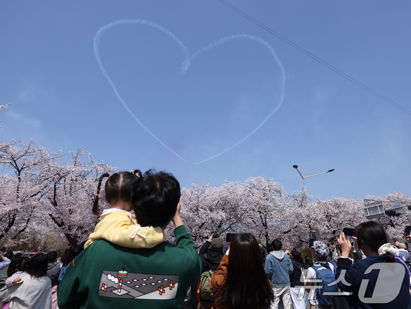 (서울=뉴스1) 박지혜 기자 = 시민들이 5일 오후 서울 여의도 봄꽃축제 메인 행사장 상공에 공군 특수 비행팀 ‘블랙이글스’가 그린 하트를 바라보고 있다. 2026.4.5/뉴스1