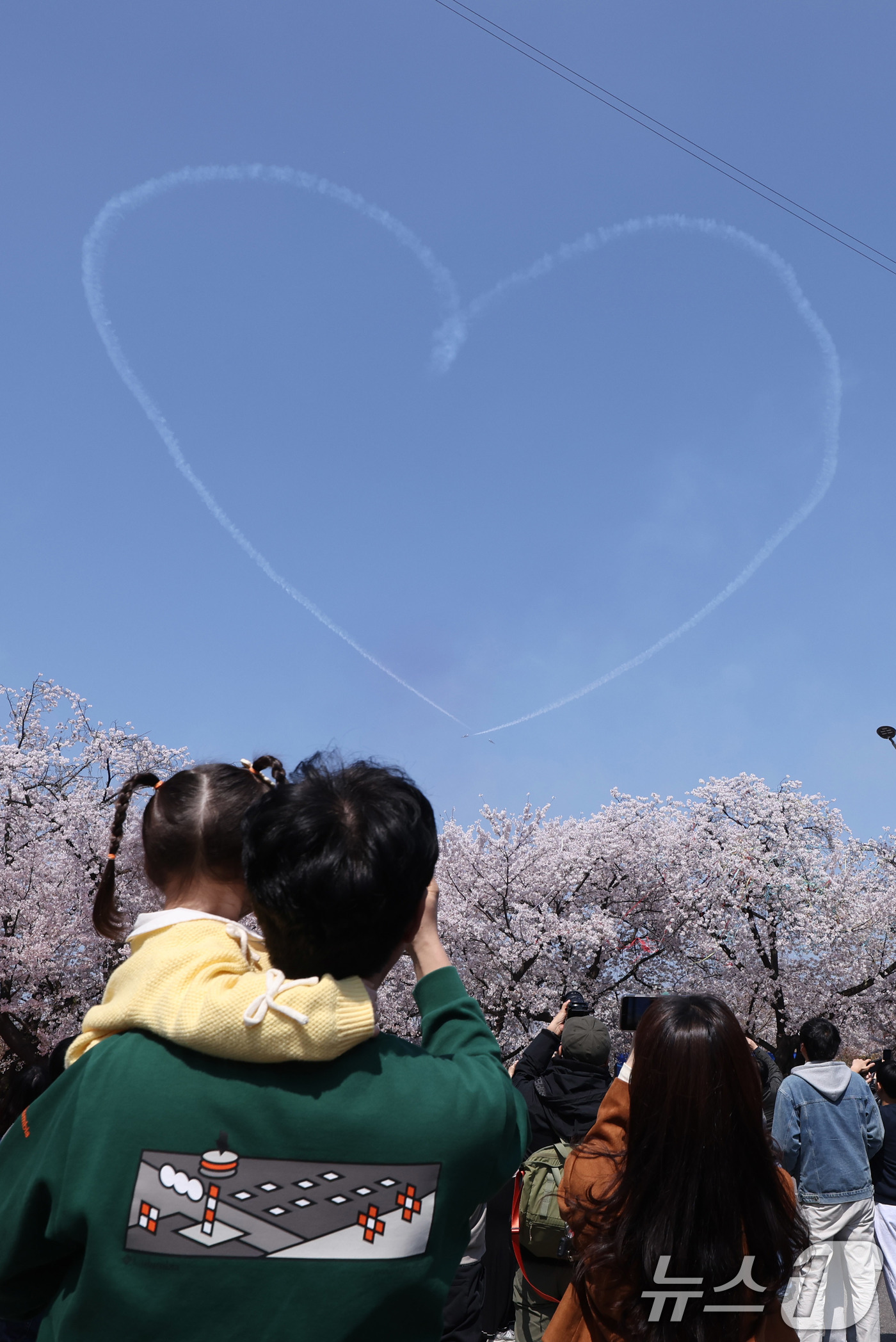 (서울=뉴스1) 박지혜 기자 = 시민들이 5일 오후 서울 여의도 봄꽃축제 메인 행사장 상공에 공군 특수 비행팀 ‘블랙이글스’가 그린 하트를 바라보고 있다. 2026.4.5/뉴스1