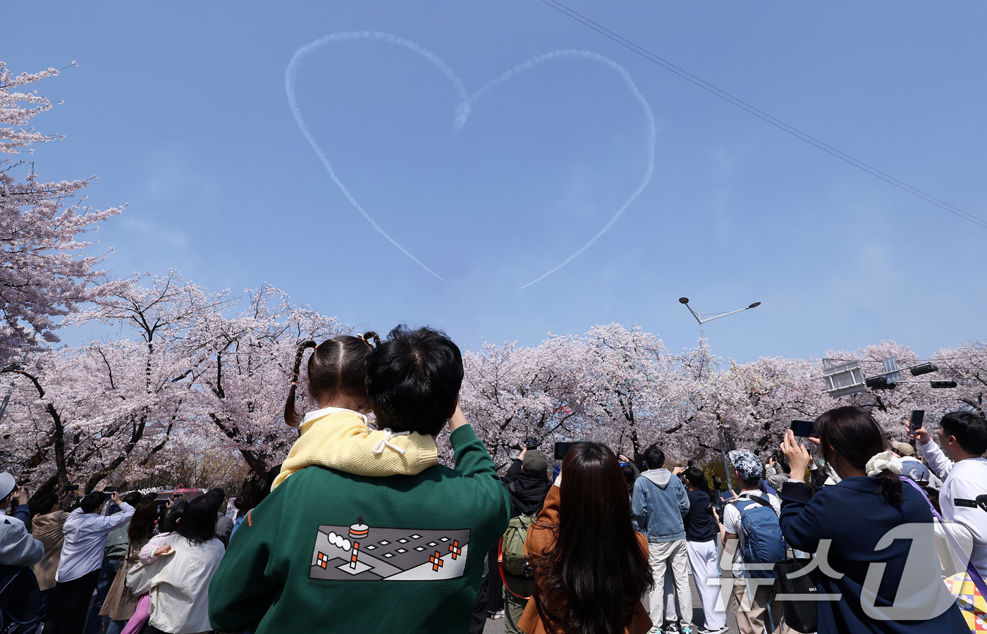 (서울=뉴스1) 박지혜 기자 = 시민들이 5일 오후 서울 여의도 봄꽃축제 메인 행사장 상공에 공군 특수 비행팀 ‘블랙이글스’가 그린 하트를 바라보고 있다. 2026.4.5/뉴스1