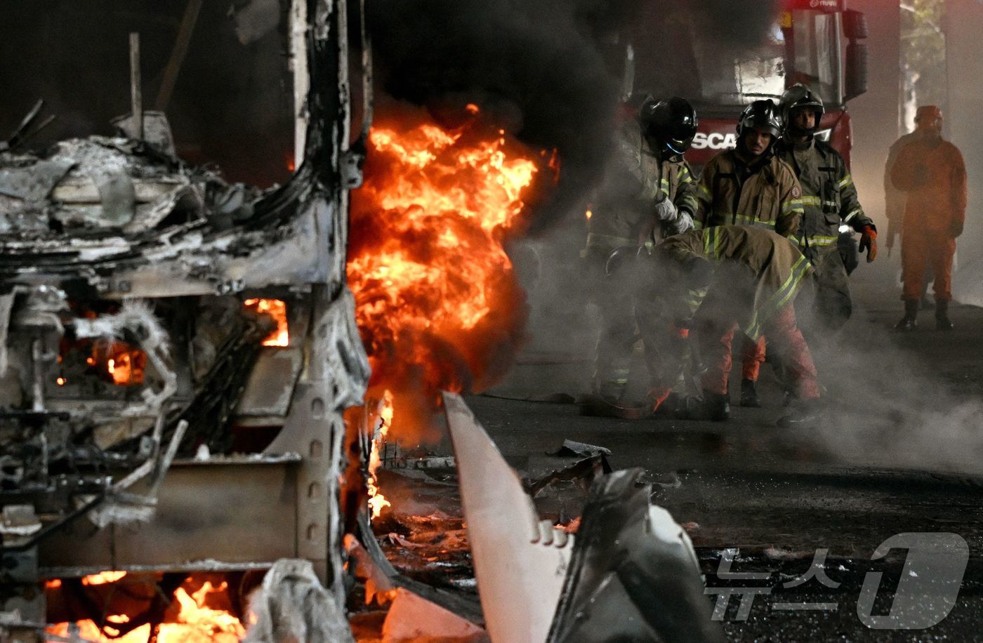 본문 이미지 - 18일(현지시간) 브라질 리우데자네이루 중심부에서 경찰 작전 중 마약 밀매업자들이 방화한 것으로 추정되는 버스의 불을 끄기 위해 소방관들이 가정용 소화기를 사용하며 사투를 벌이고 있다. 2026.03.18.ⓒ AFP=뉴스1