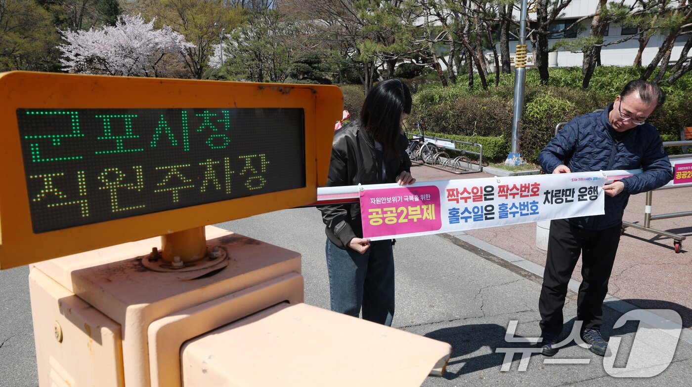 본문 이미지 - 공공기관 승용차 2부제 시행을 하루 앞둔 7일 경기 군포시 금정동 군포시청 직원주차장에서 직원들이 공공기관 2부제를 알리는 현수막을 부착하고 있다. 2026.4.7 ⓒ 뉴스1 김영운 기자