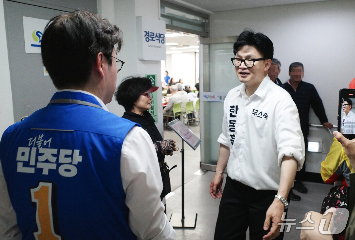 본문 이미지 - 부산 북구갑 보궐선거에 출마하는 한동훈 무소속 후보가 12일 부산 북구 덕천종합사회복지관에서 짜장면 배식 봉사를 하던 중 하정우 더불어민주당 후보와 인사를 나누고 있다. 2026.05.12 ⓒ 뉴스1 김세정 기자