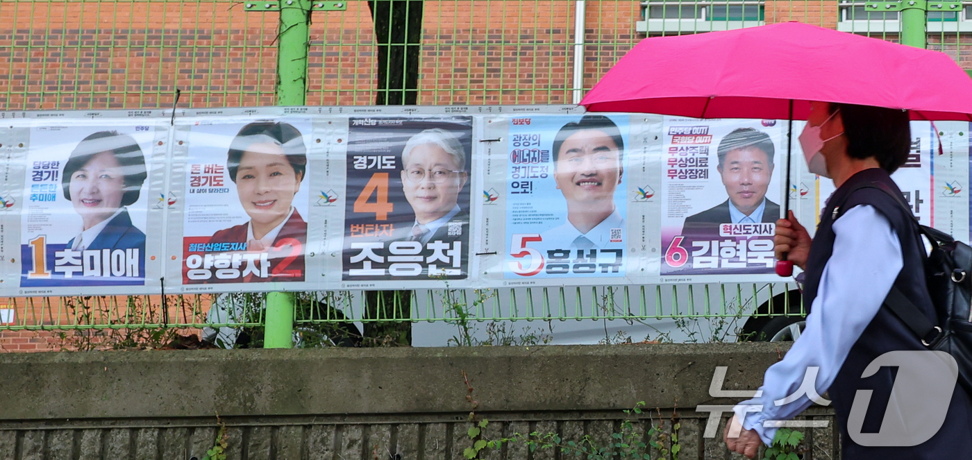 (수원=뉴스1) 안은나 기자 = 제9회 전국동시지방선거 공식 선거운동이 시작된 21일 경기 수원시 팔달구 율현중학교 앞에서 한 시민이 경기도지사 후보 선거벽보 앞을 지나고 있다. …