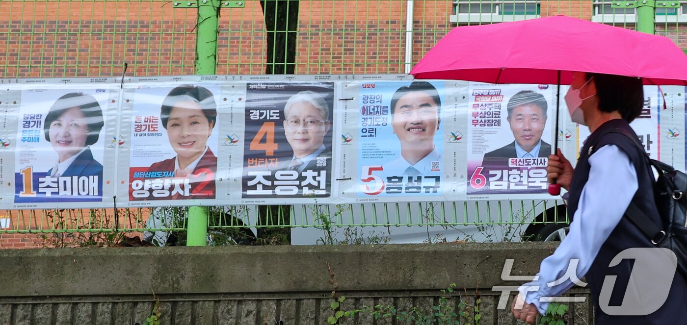 본문 이미지 - 제9회 전국동시지방선거 공식 선거운동이 시작된 21일 경기 수원시 팔달구 율현중학교 앞에서 한 시민이 경기도지사 후보 선거벽보 앞을 지나고 있다. 2026.5.21 ⓒ 뉴스1 안은나 기자