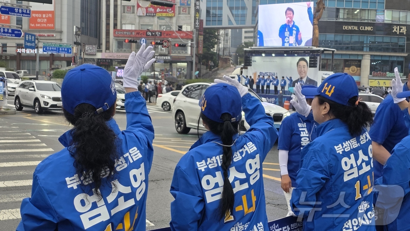 (천안=뉴스1) 이시우 기자 = 21일 천안시 서북구 일봉산사거리에서 열린 더불어민주당 합동 출정식에서 민주당 선거운동원들이 출근 중 시민들을 향해 손을 흔들고 있다.  2026. …
