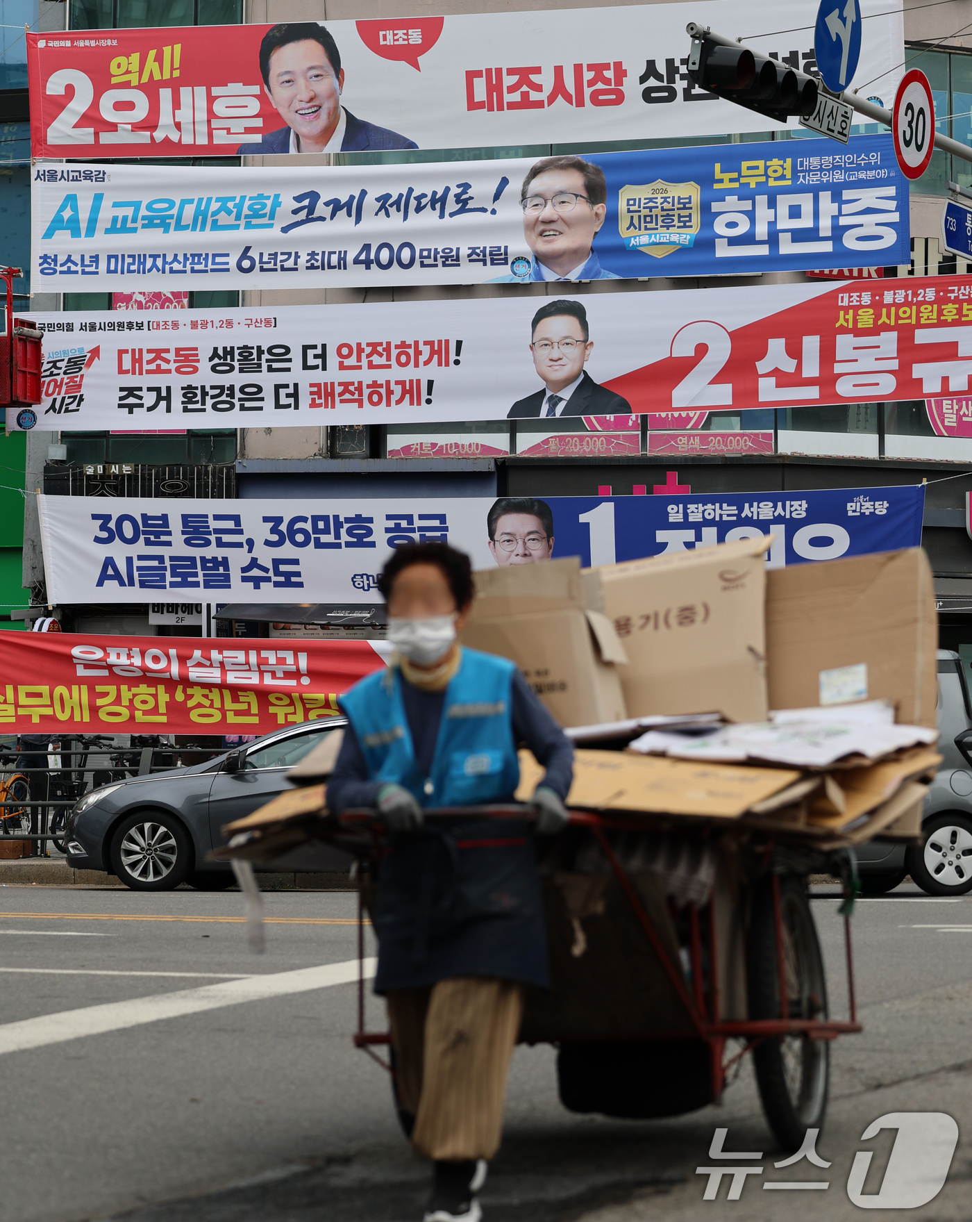(서울=뉴스1) 오대일 기자 = 6·3 지방선거 공식 선거운동이 시작된 21일 서울 은평구의 한 거리에서 폐지 수레를 끄는 할머니가 여야 후보자들의 선거 현수막 앞을 힘겹게 지나고 …